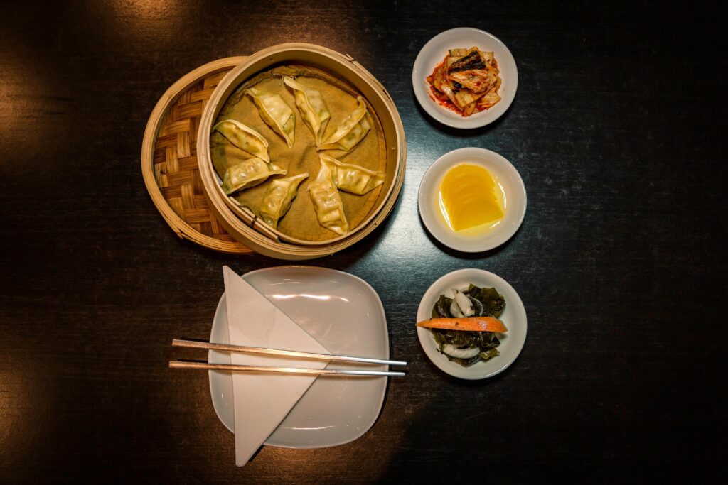 Steamed dumplings with side dishes and chopsticks on a dark table, perfect for culinary themes.