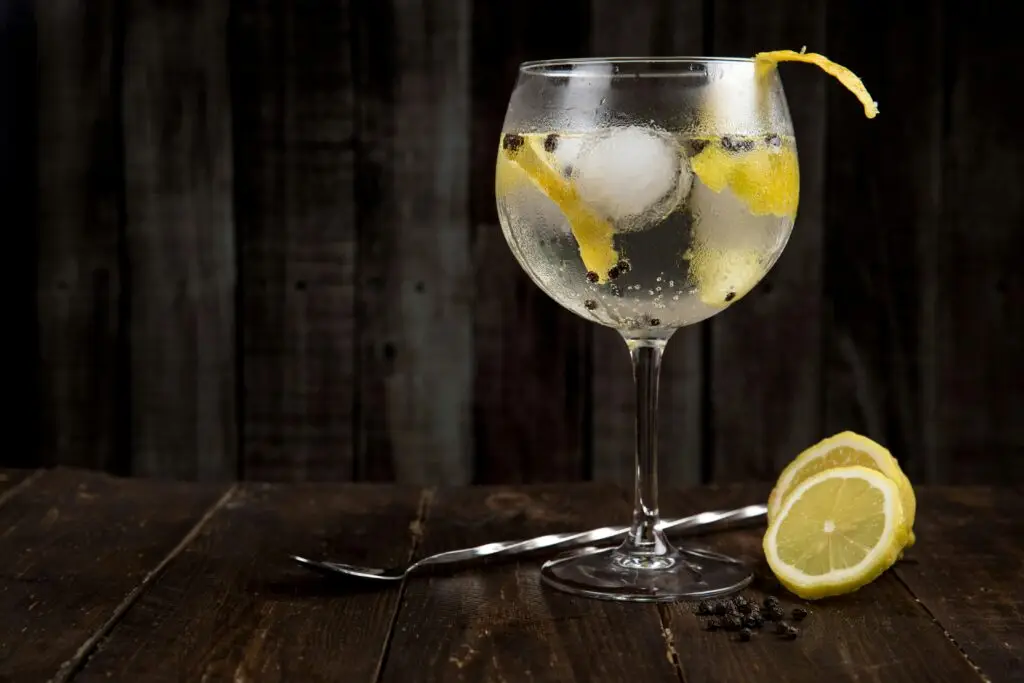 A close-up of a refreshing gin cocktail with lemon slices on a rustic wooden table, perfect for summer.